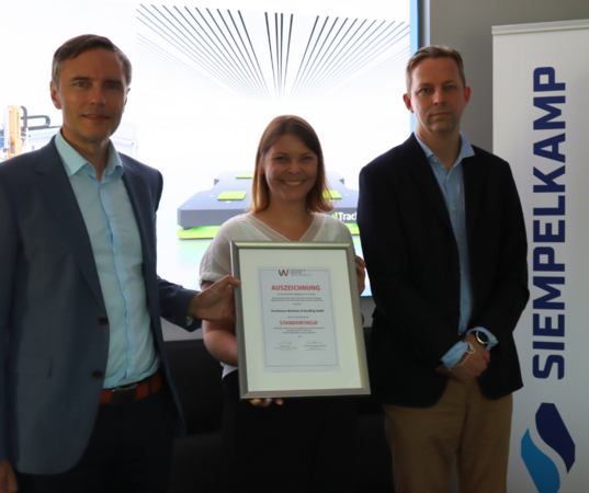 Die Geschäftsführer Torsten Ristow und Stefan Rehling (Siempelkamp Transport Systems GmbH) bekommen die Auszeichnung „Standortheld“ von Anna Niehaus (pro Wirtschaft GT) überreicht.