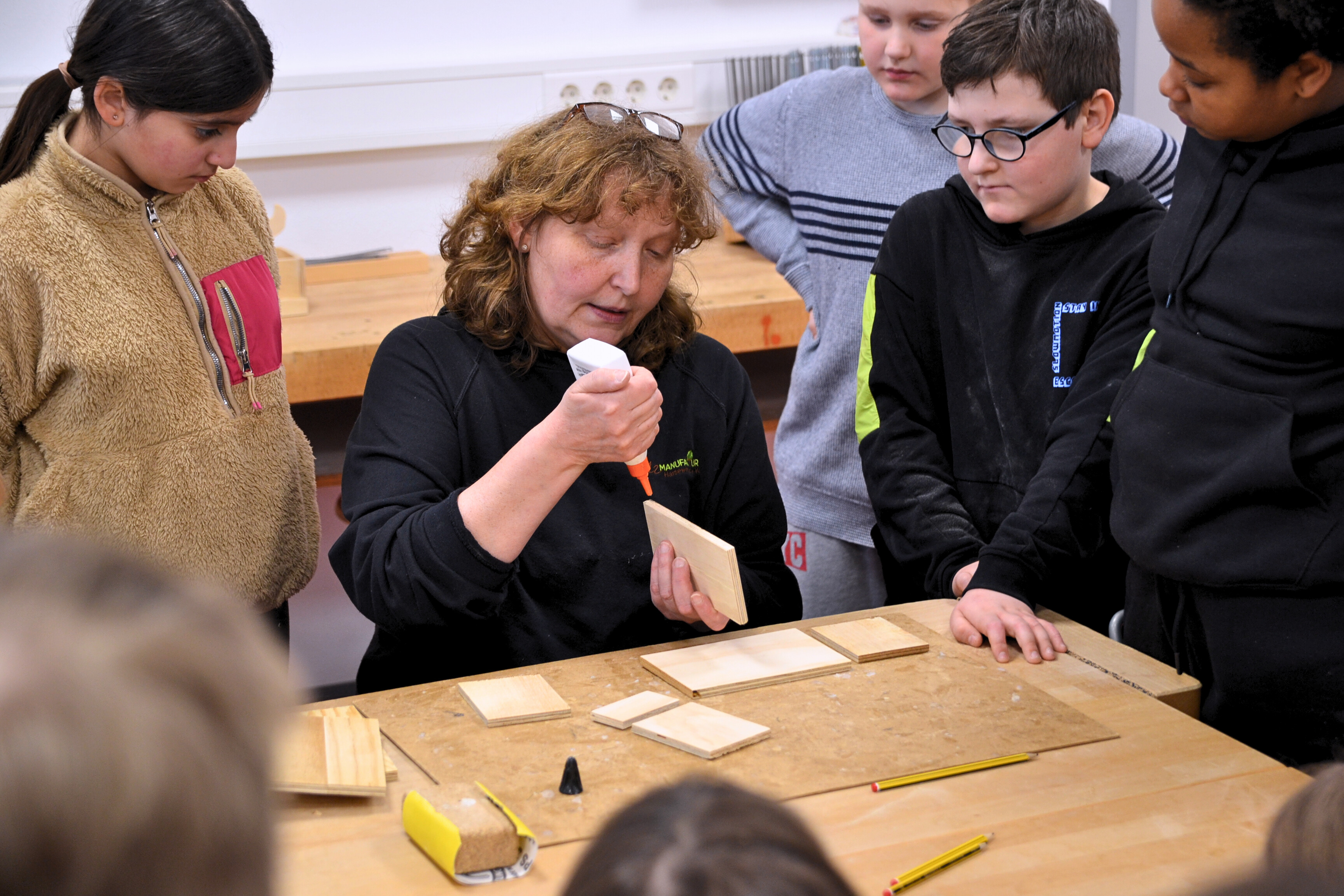 Werkstattleiterin Ute Delbrügge zeigt den Besucherinnen und Besuchern aus Versmold, wie man den Leim korrekt aufträgt. 