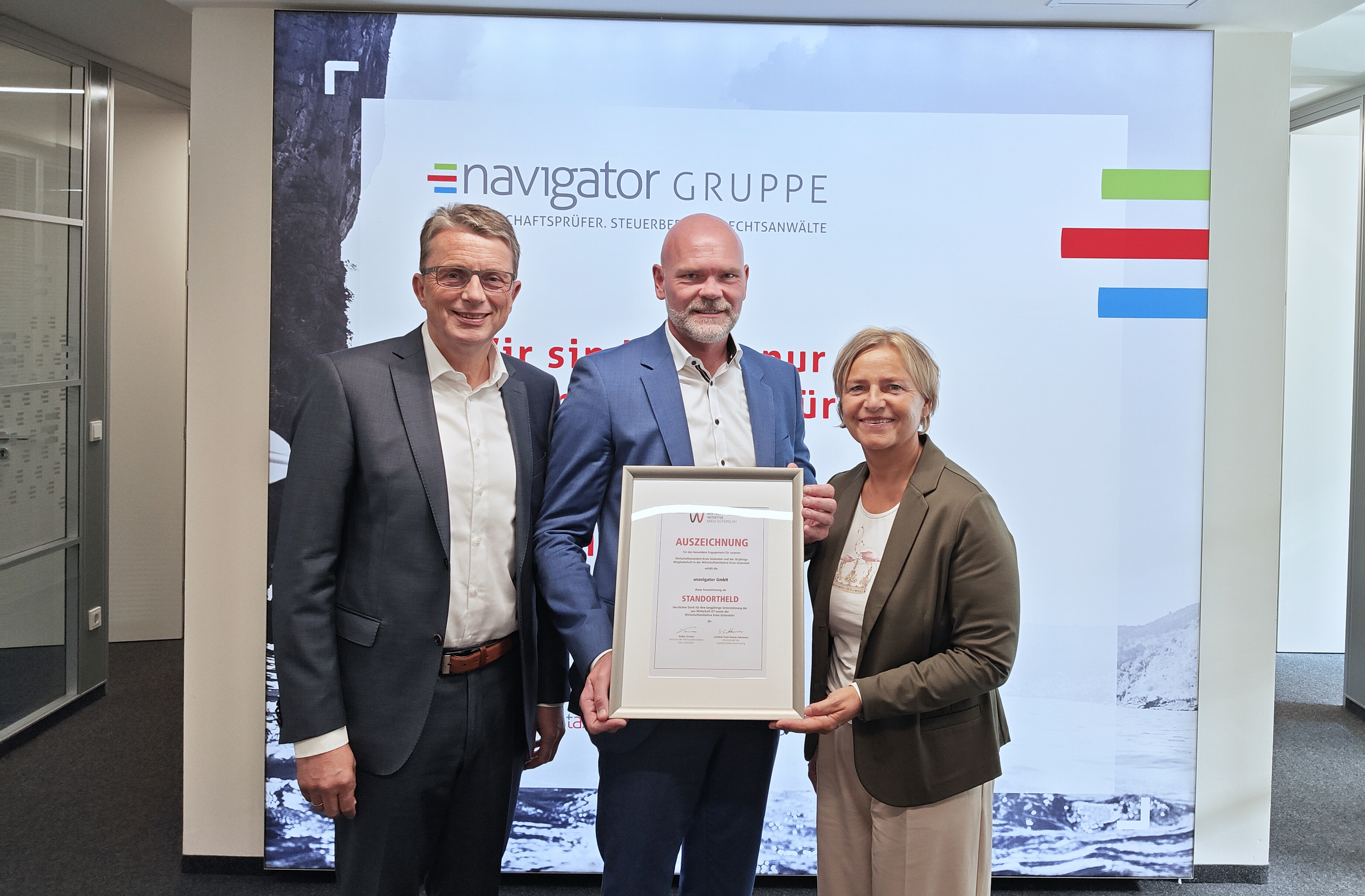 Michael Deitert (Vorstand Wirtschaftsinitiative Kreis Gütersloh, links) und Nikola Weber (Geschäftsführerin pro Wirtschaft GT), zeichneten Mario Frisch und die navigator Gruppe als ‚Standorthelden‘ aus.